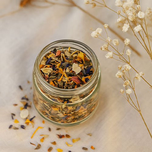 Gläschen mit Räucherwerk inmitten von Blüten